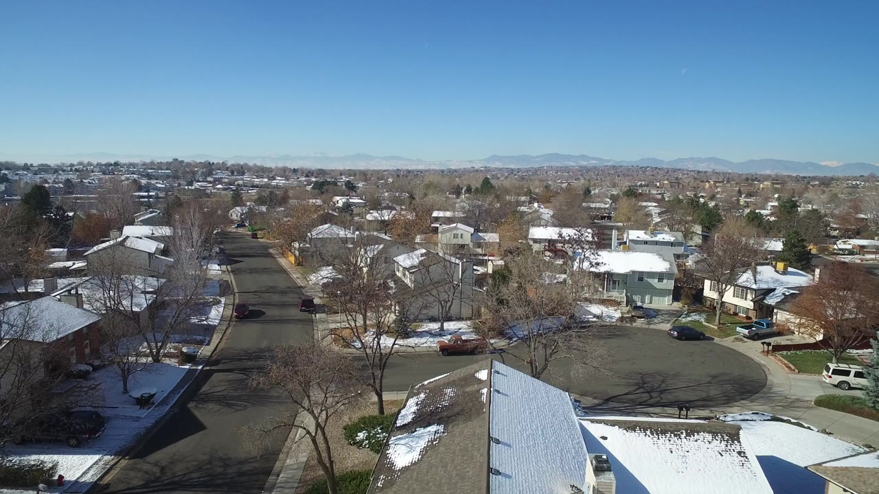 Aerial view over snow-dusted suburban houses and curved roads under blue sky.