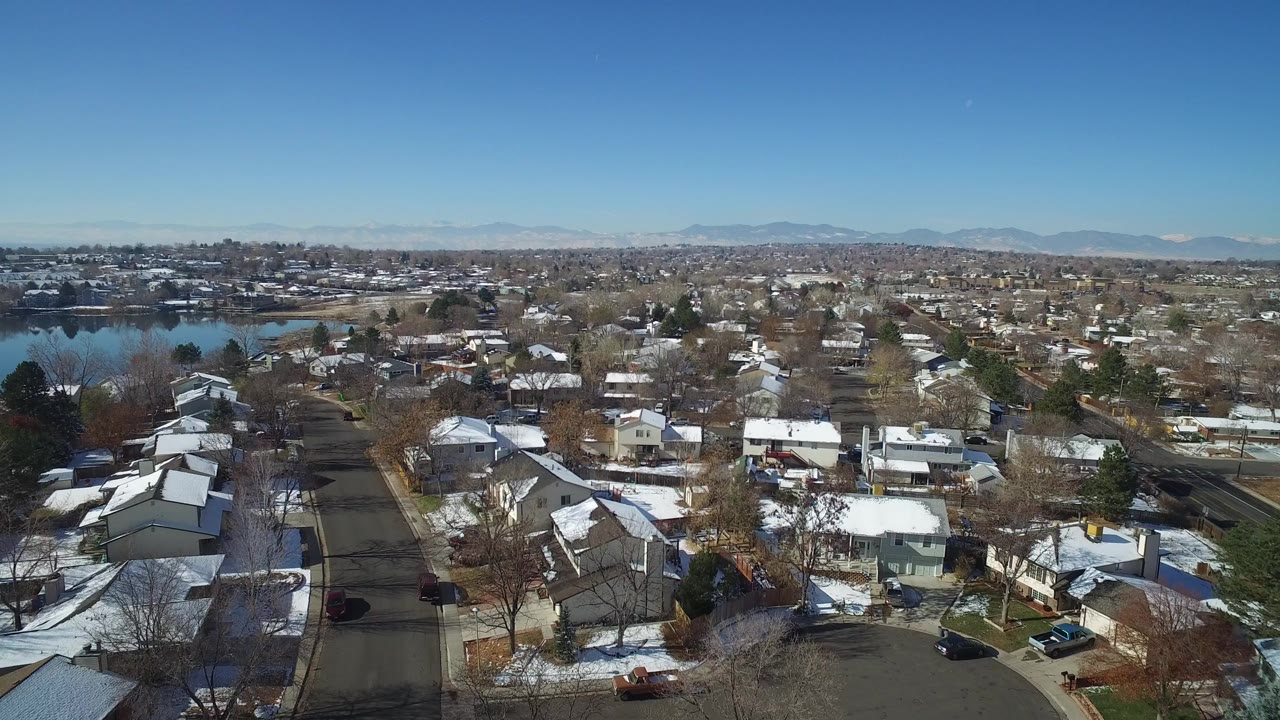 Aerial view of snowy suburban homes beside a lake under a clear sky.