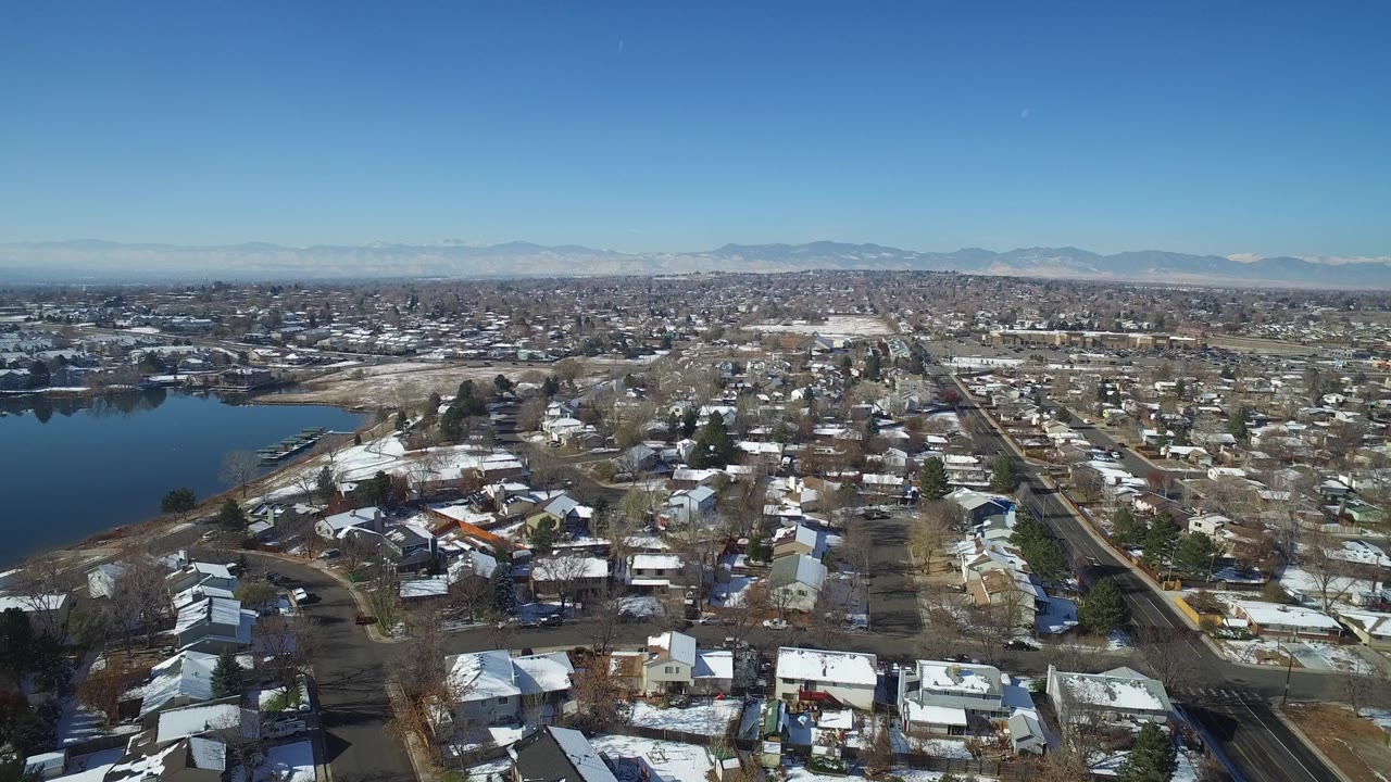 Drone-like view across a residential area with water at left and mountains beyond.