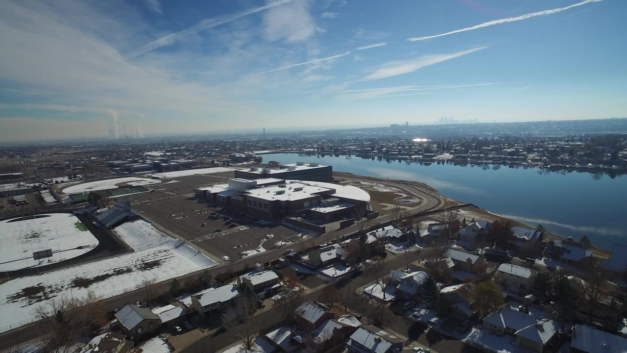 Aerial view of snow-dusted homes, roads, a sports arena, and water under a blue sky.
