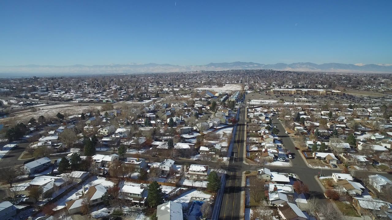 Aerial view of snow-dusted suburban homes and streets under a blue sky.