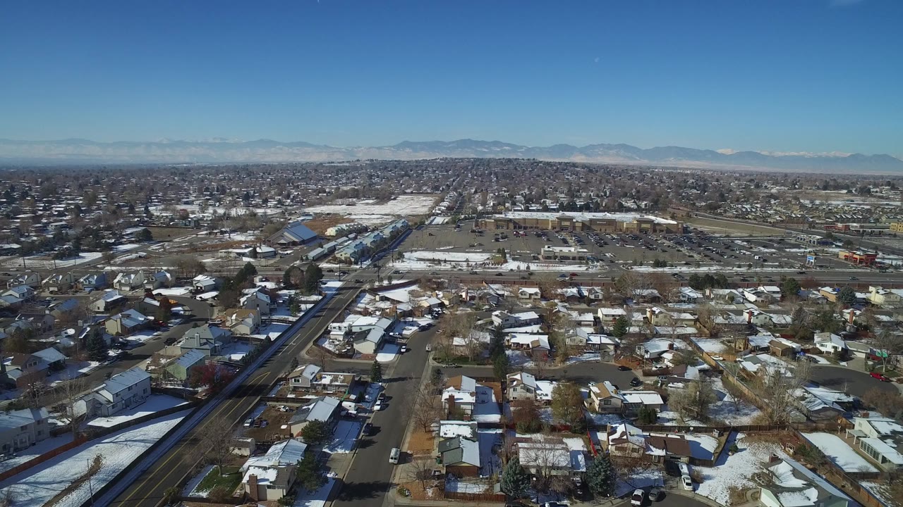 Aerial view over snowy residential streets and rooftops with mountains on the horizon.