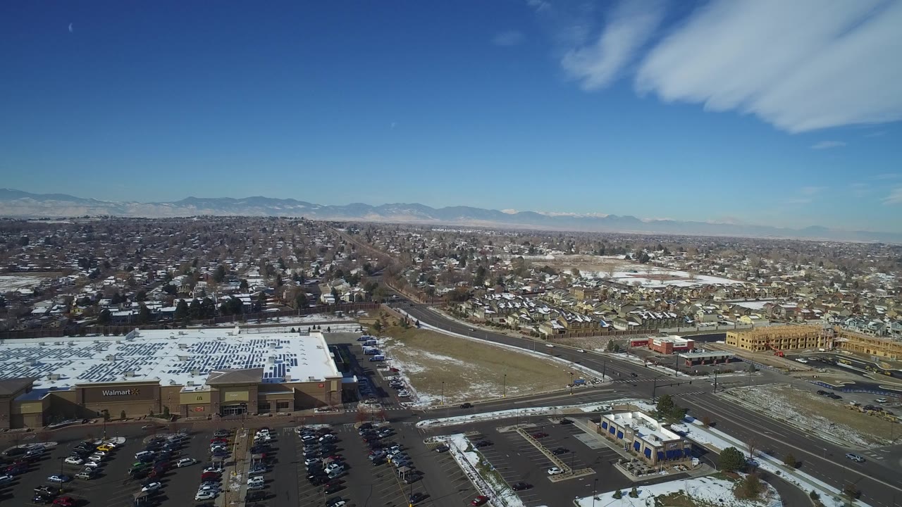 One second into the clip, the Hidden Lake aerial keeps the large commercial roof and parking lots low in frame while the residential grid and mountain horizon fill the distance, with no visible people.