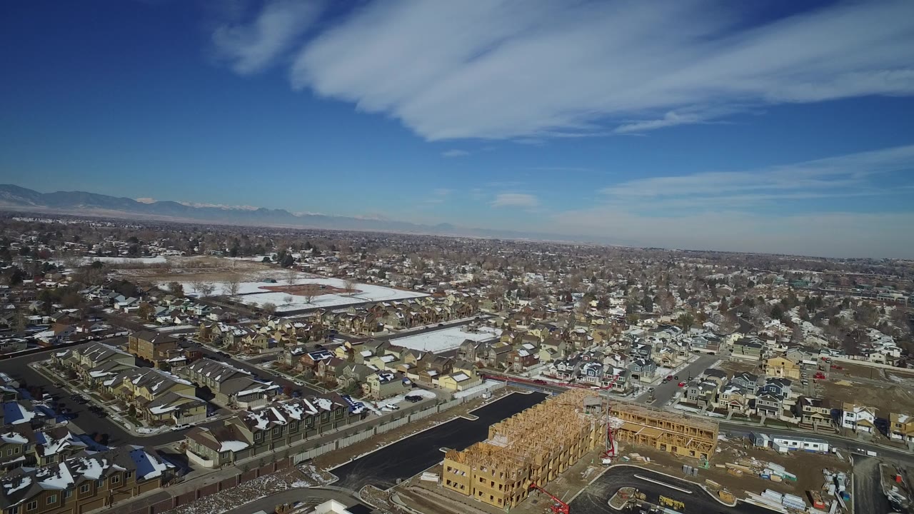 Opening aerial frame over Hidden Lake, Colorado with residential streets, houses, a pale lake or ice area left of center, distant mountains, and no visible people.
