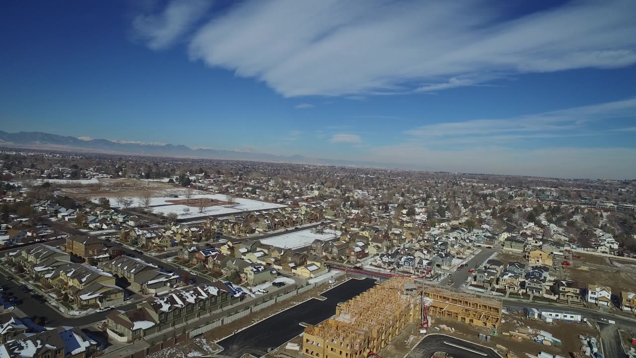 Drone-height view across houses, a road junction, pale lake surface, and a wide sky.