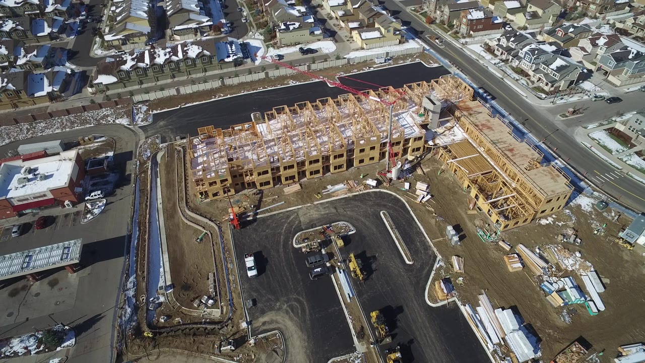 High-angle construction site with roads, material piles, and nearby homes.