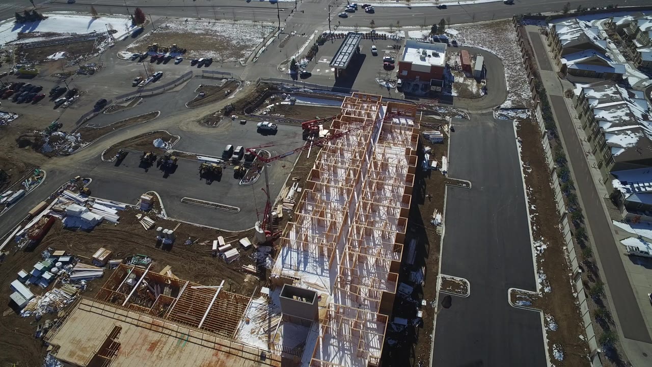 Aerial view of wood-framed construction beside paved roads and parked cars.