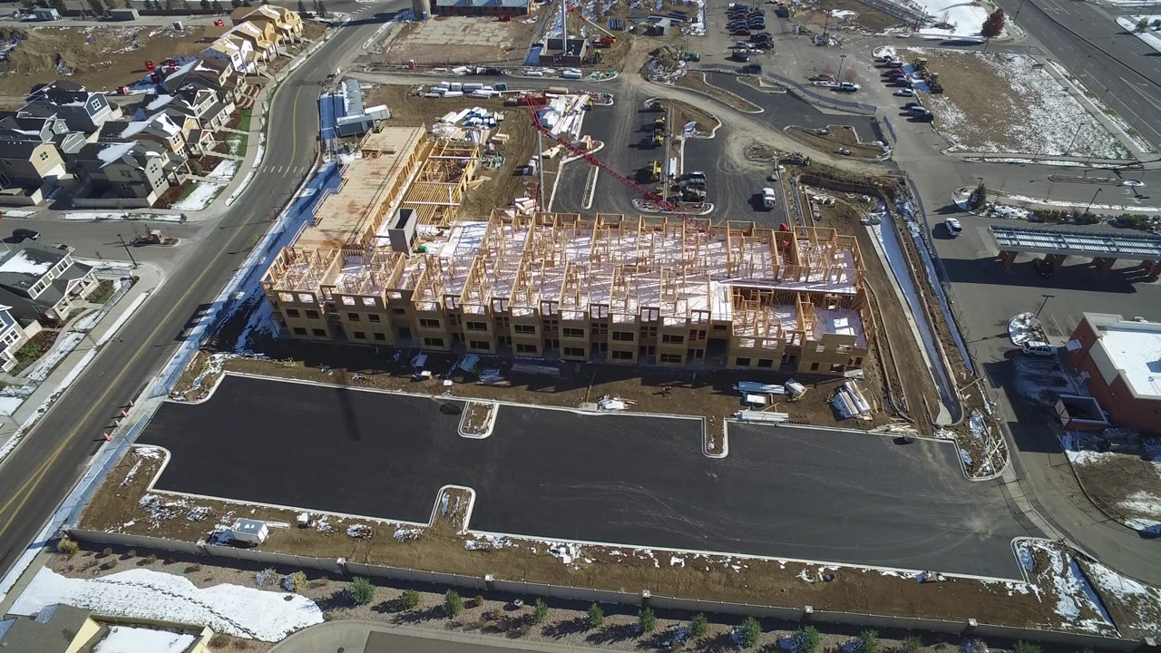 Aerial view of a wood-framed building under construction beside a paved lot.