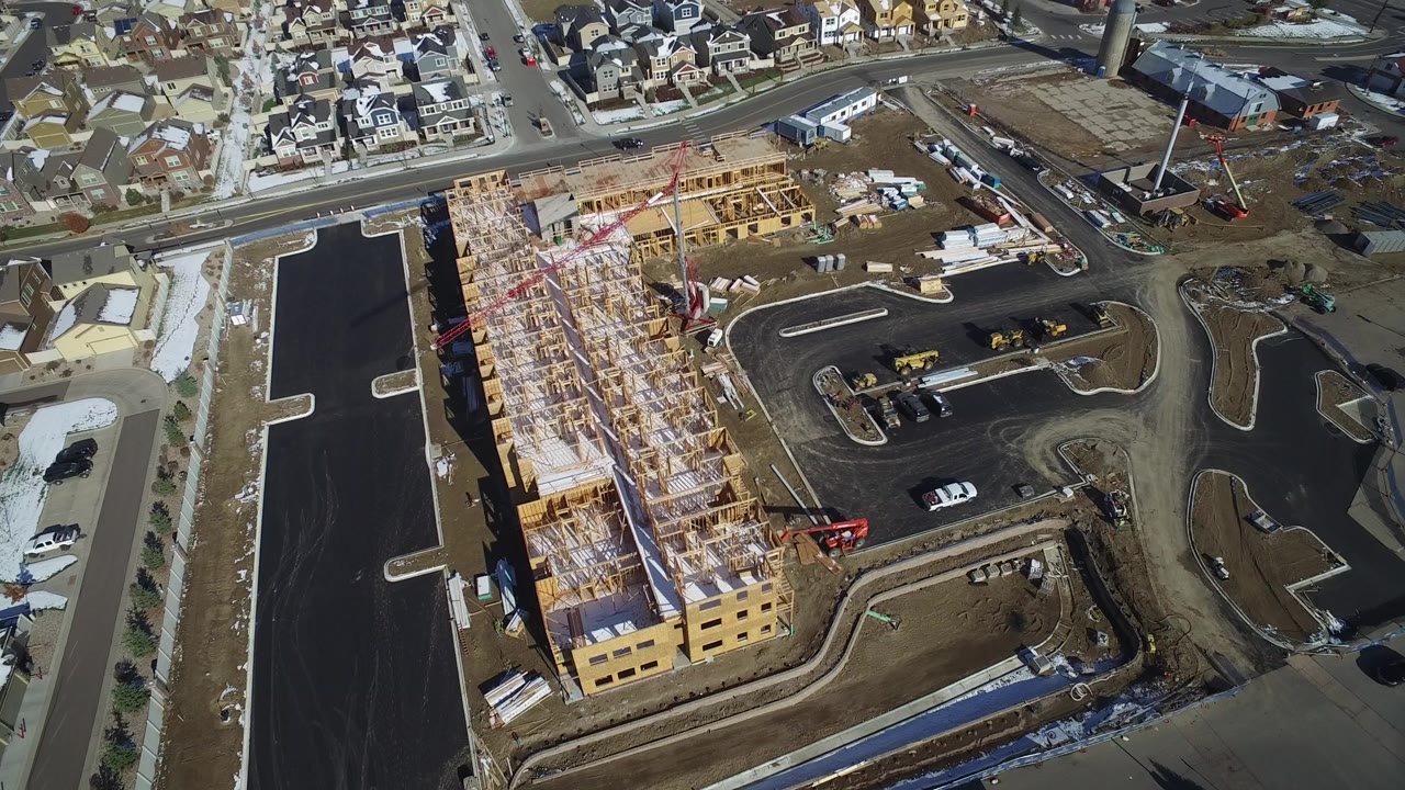 Aerial view of an apartment construction site beside paved roads and homes.