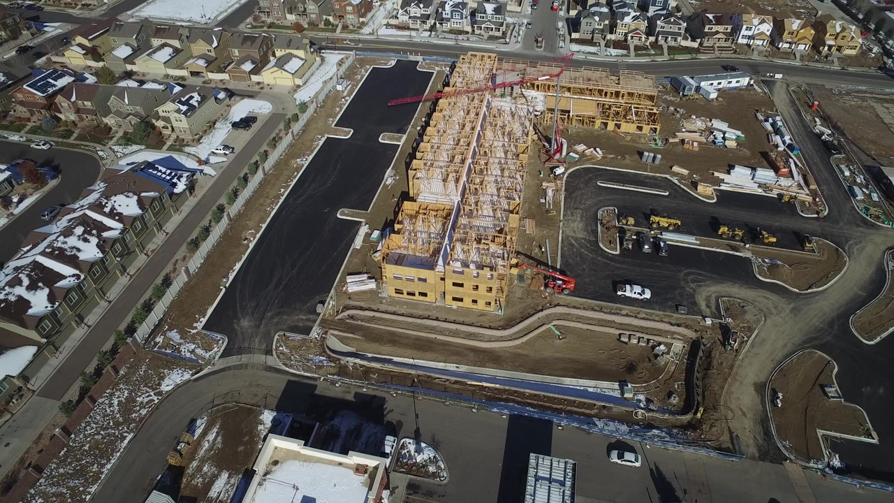 Aerial view of a wood-framed construction site beside suburban roads.
