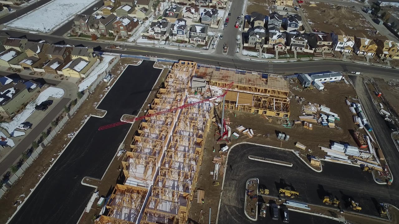 Aerial construction site with wood framing, roads, homes, and snow patches.