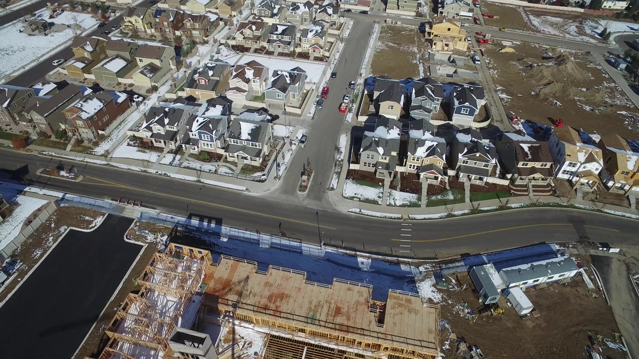 High aerial frame over Hidden Lake, Colorado showing snow-dusted private homes, a curved road, a partially framed construction site, open lots, parked cars, and no visible people.