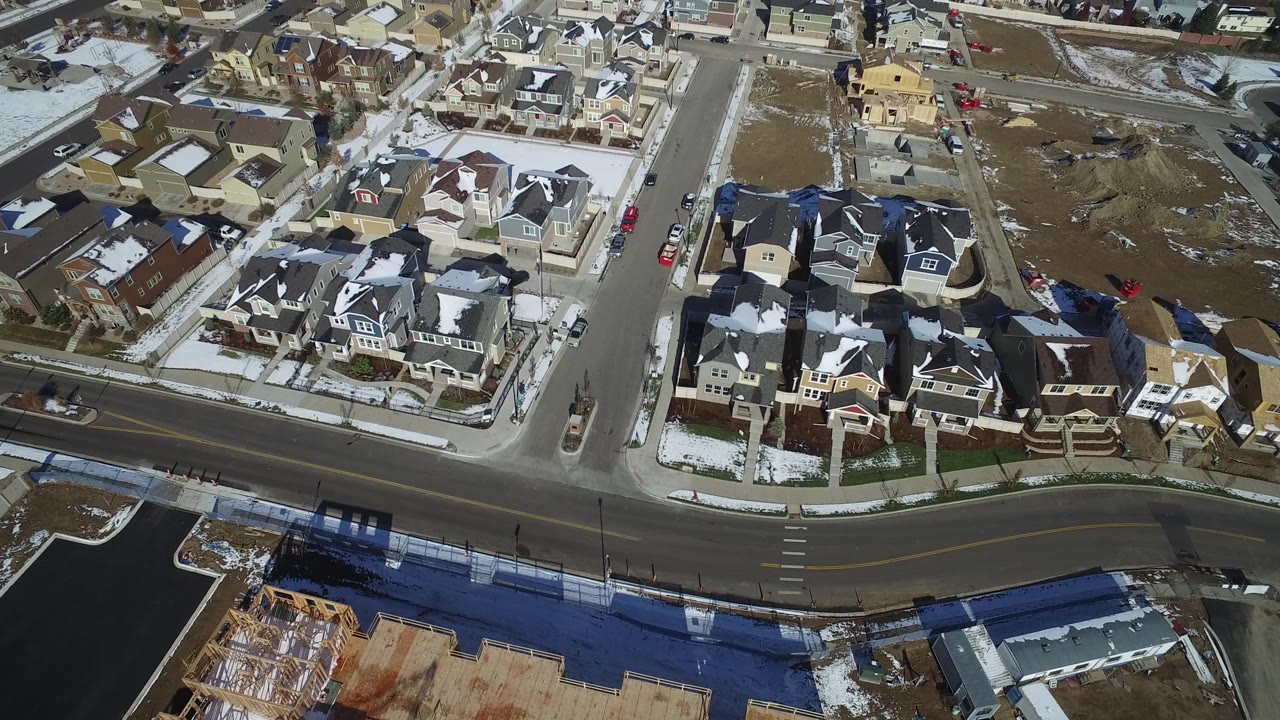 Overhead subdivision view with houses, roads, snow, and undeveloped land.