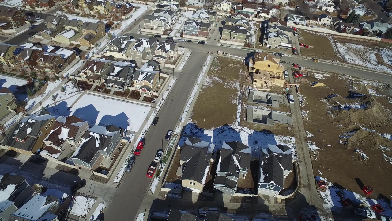 Drone view across Hidden Lake, Colorado residential blocks, showing snow-edged lawns, parked vehicles, brown lots, and no visible people.