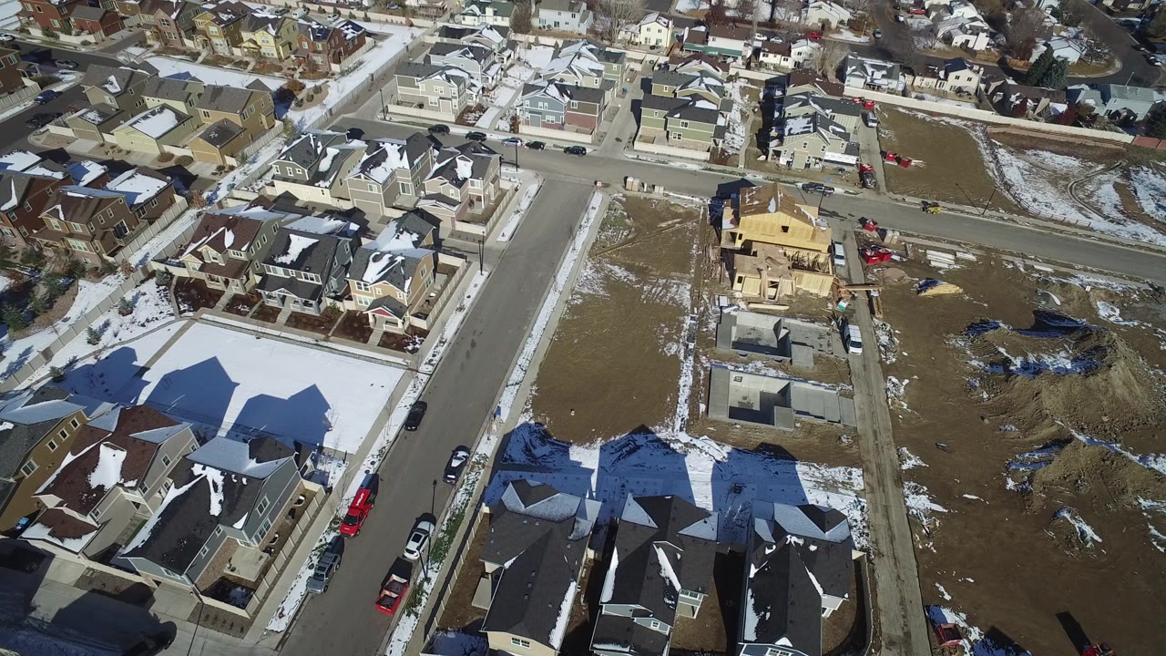 Overhead neighborhood view with houses, roads, snow patches, and open land.