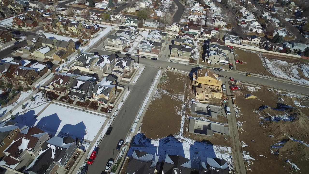 Aerial view of suburban houses, streets, open lots, and snow patches.