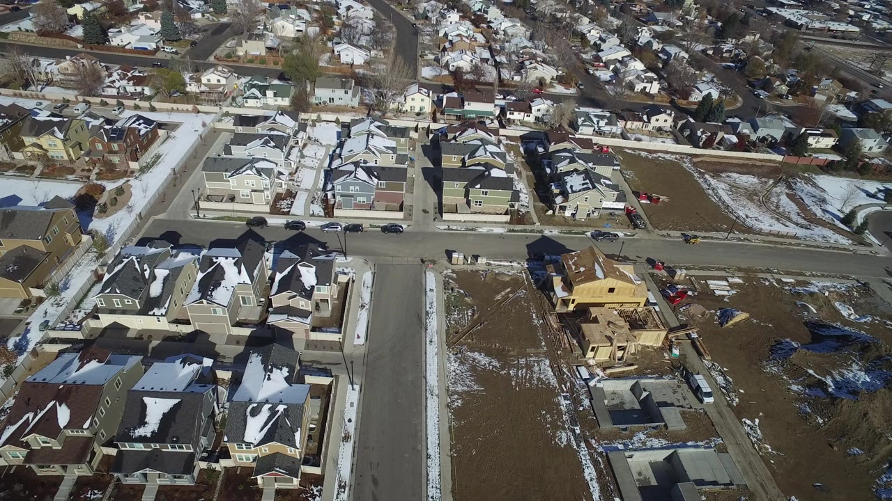 Aerial view of suburban houses, streets, snow patches, and a framed house under construction.