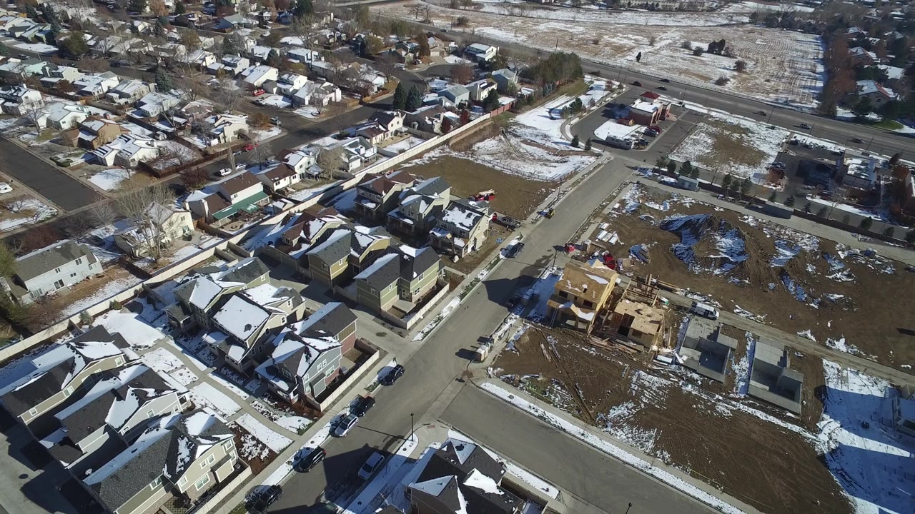 Suburban neighborhood seen from above with snow patches, rooftops, roads, and light traffic.