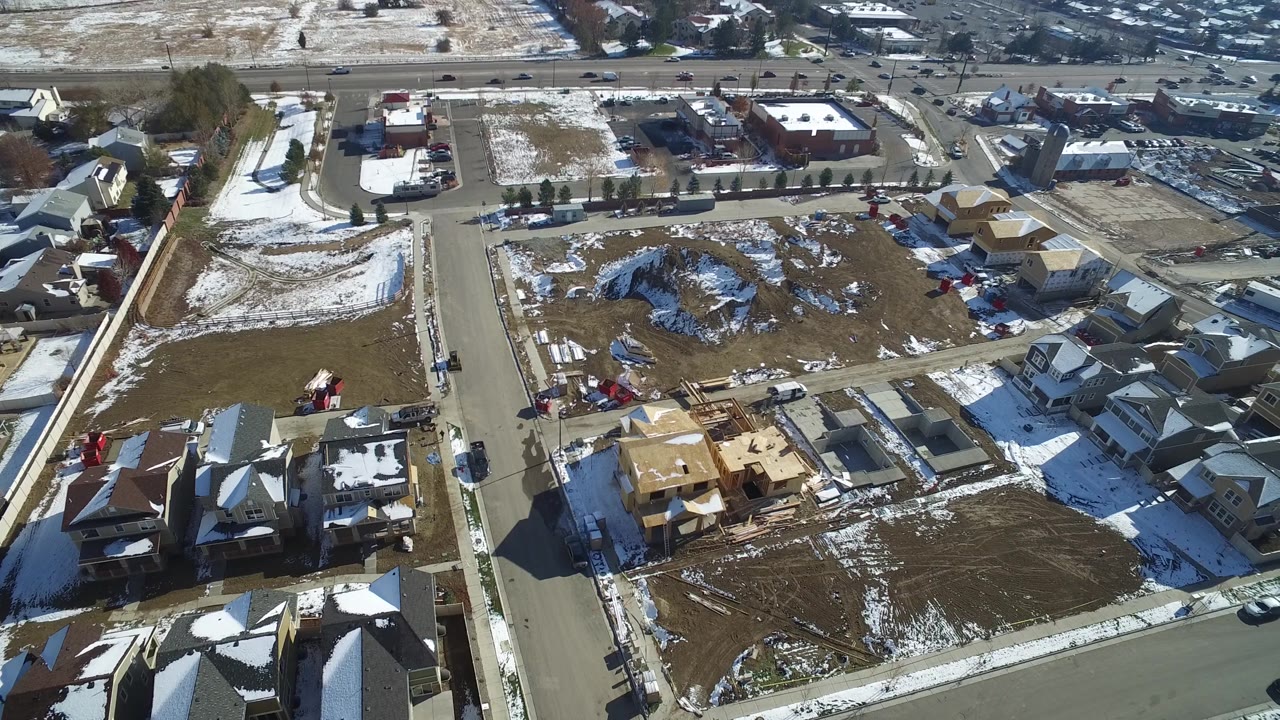 Overhead neighborhood view with homes, vacant parcels, roads, and parked cars.