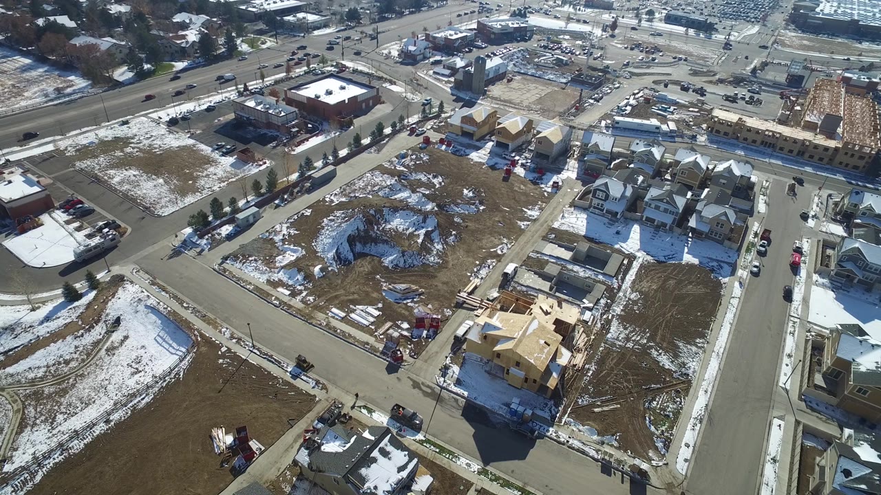 Aerial frame over Hidden Lake, Colorado with a central road, clustered homes on the right, open lots on the left, patchy snow, and no visible people.