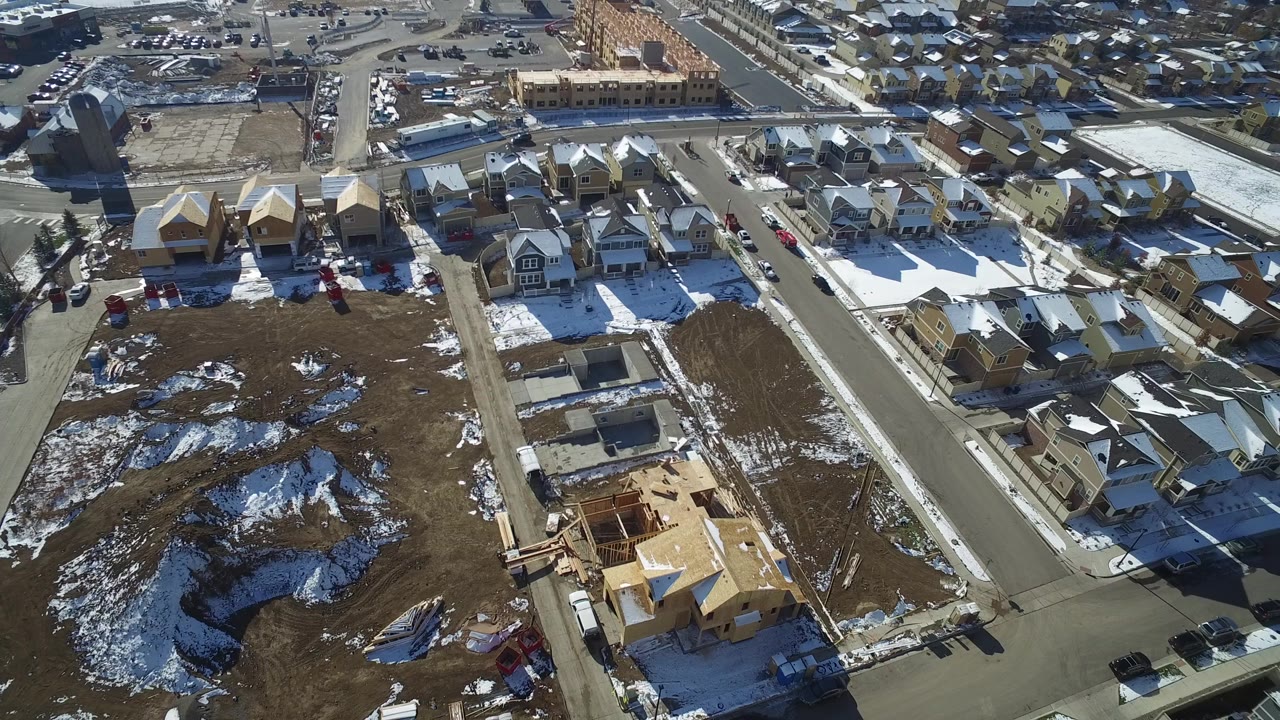 Aerial view of suburban houses, streets, snow patches, and construction lots.
