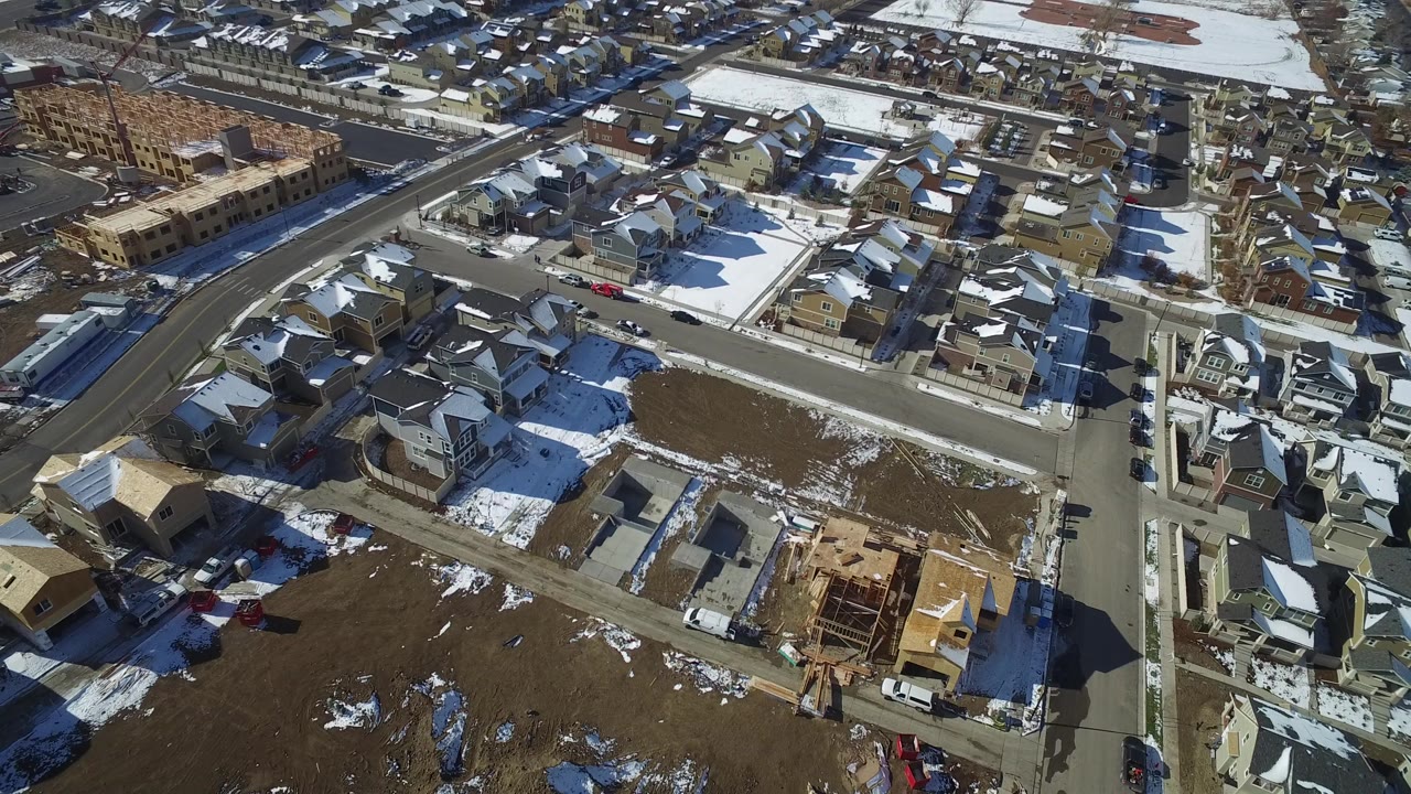 Aerial view of suburban homes, snowy lawns, streets, and a house under construction.