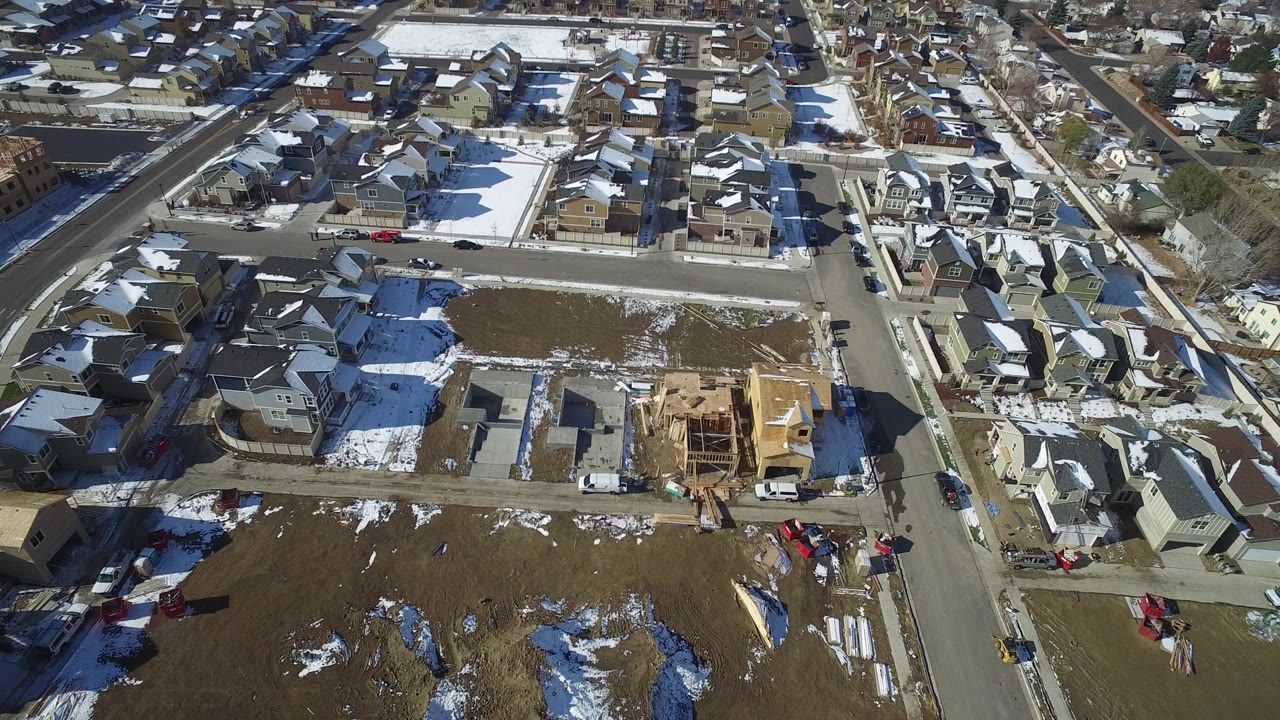 Aerial view of suburban homes, streets, snow patches, and a house under construction.