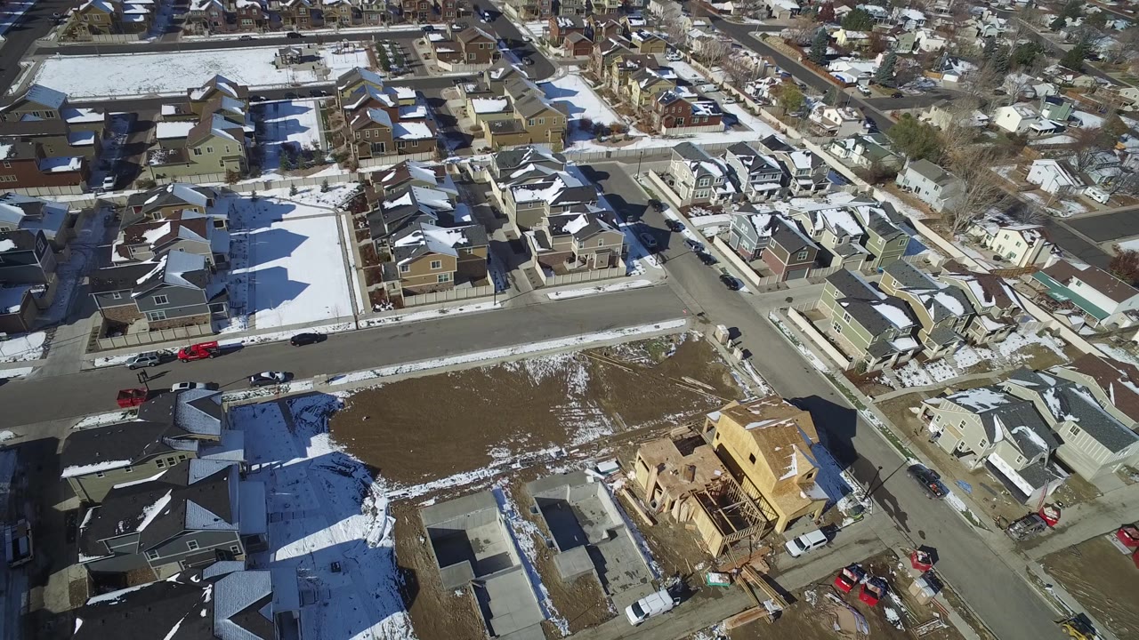 Aerial frame over Hidden Lake, Colorado with snowy rooftops, a broad residential road, parked vehicles, open lots, and no visible people.