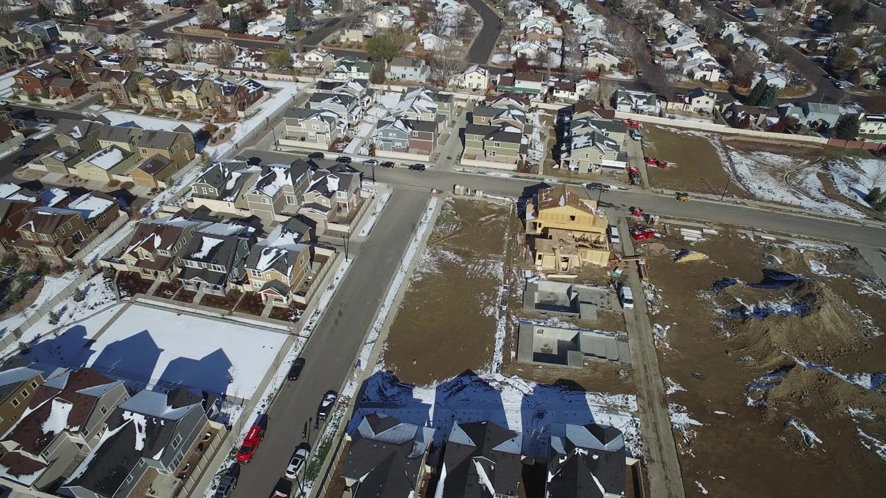 Aerial view of suburban houses, roads, snow patches, and open lots.