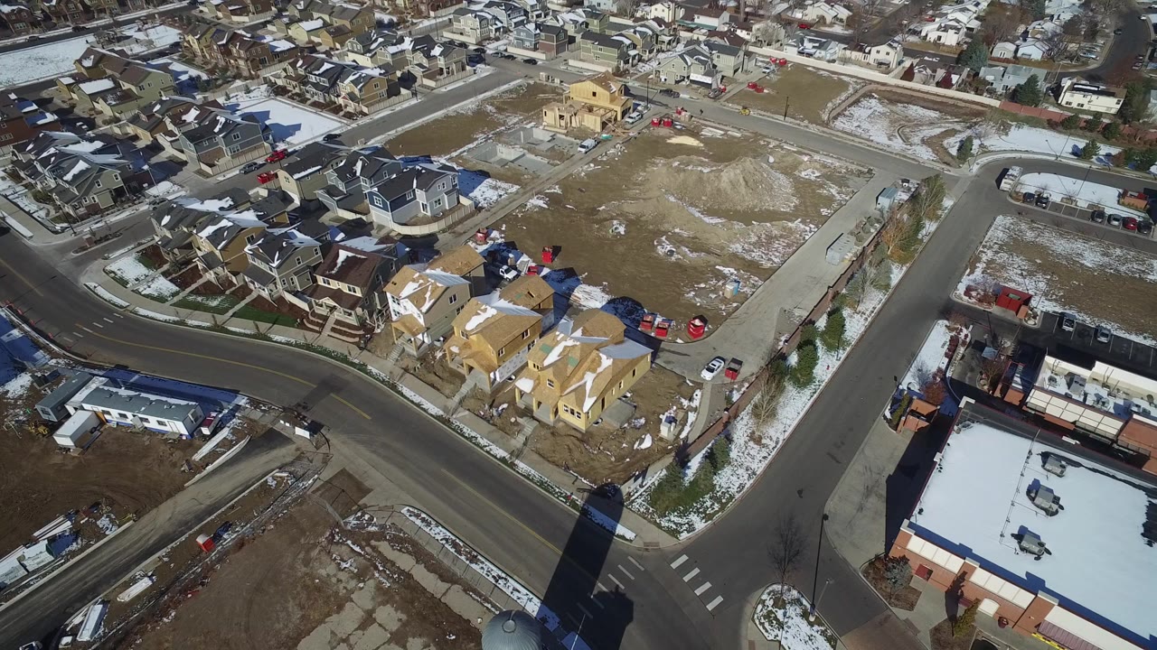 Aerial view of a road junction, houses, parking lots, and patchy snow.