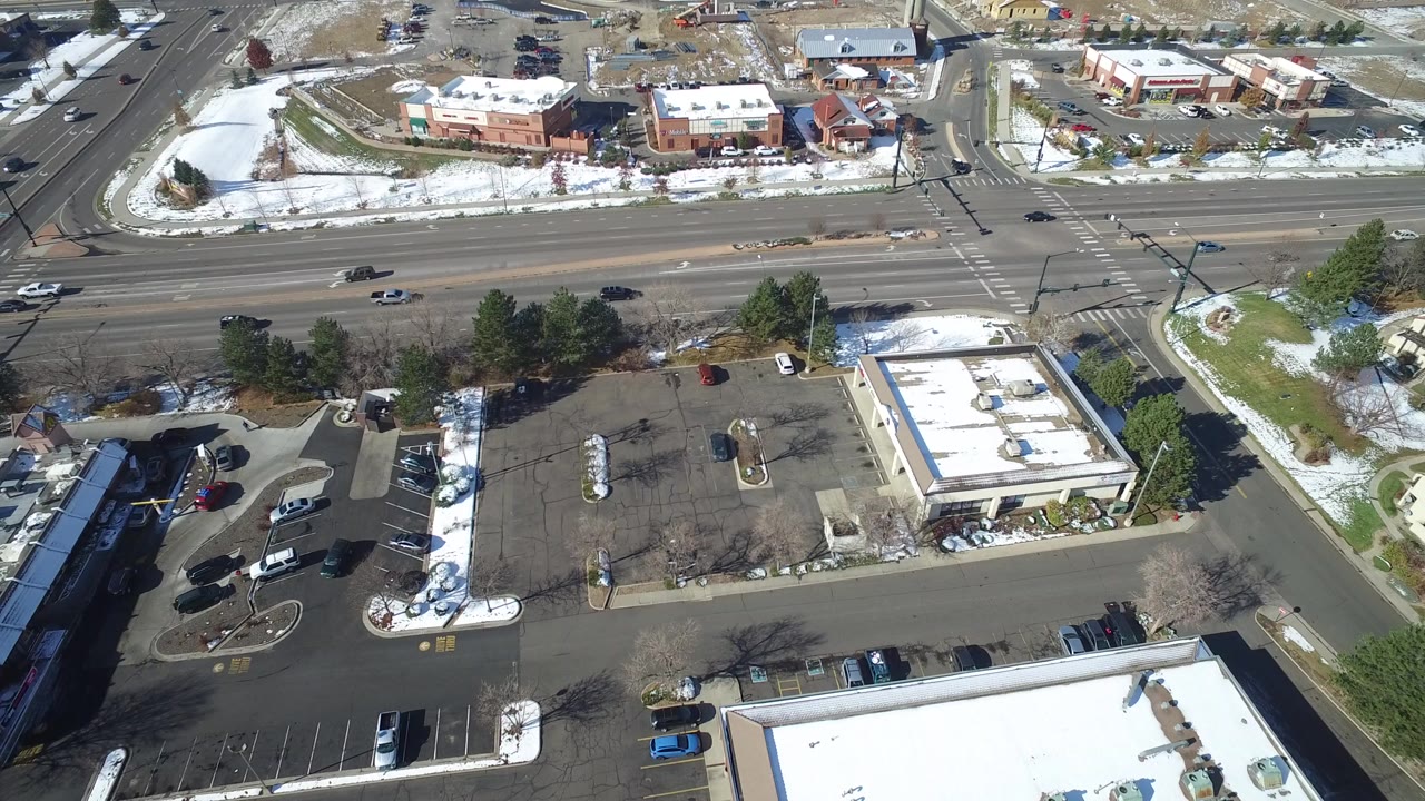 Aerial view of a sparse commercial parking lot beside a multi-lane road with snow patches.