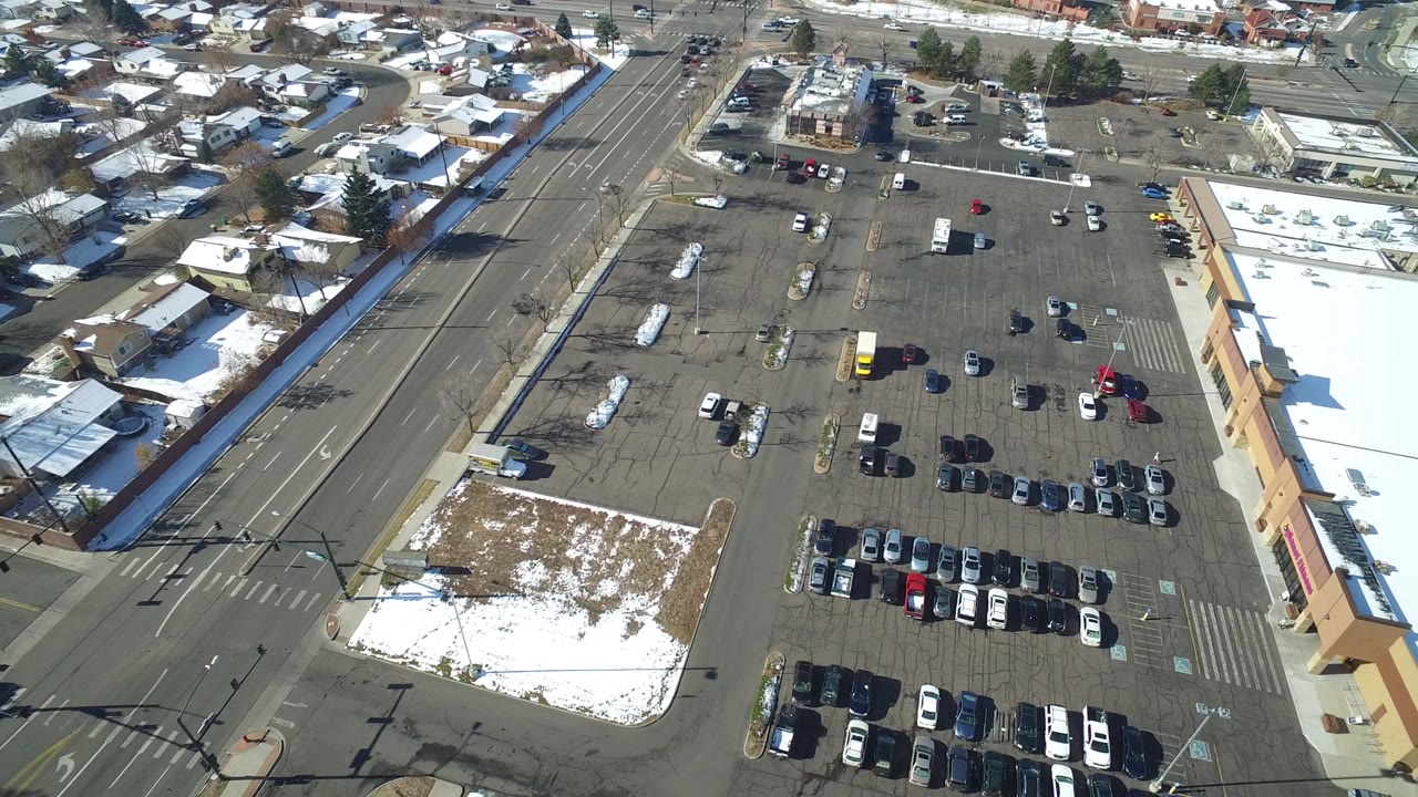 Aerial frame in Hidden Lake, Colorado with the parking lot centered, cars arranged in rows, snow on grass and roofs, and homes lining the upper edge.