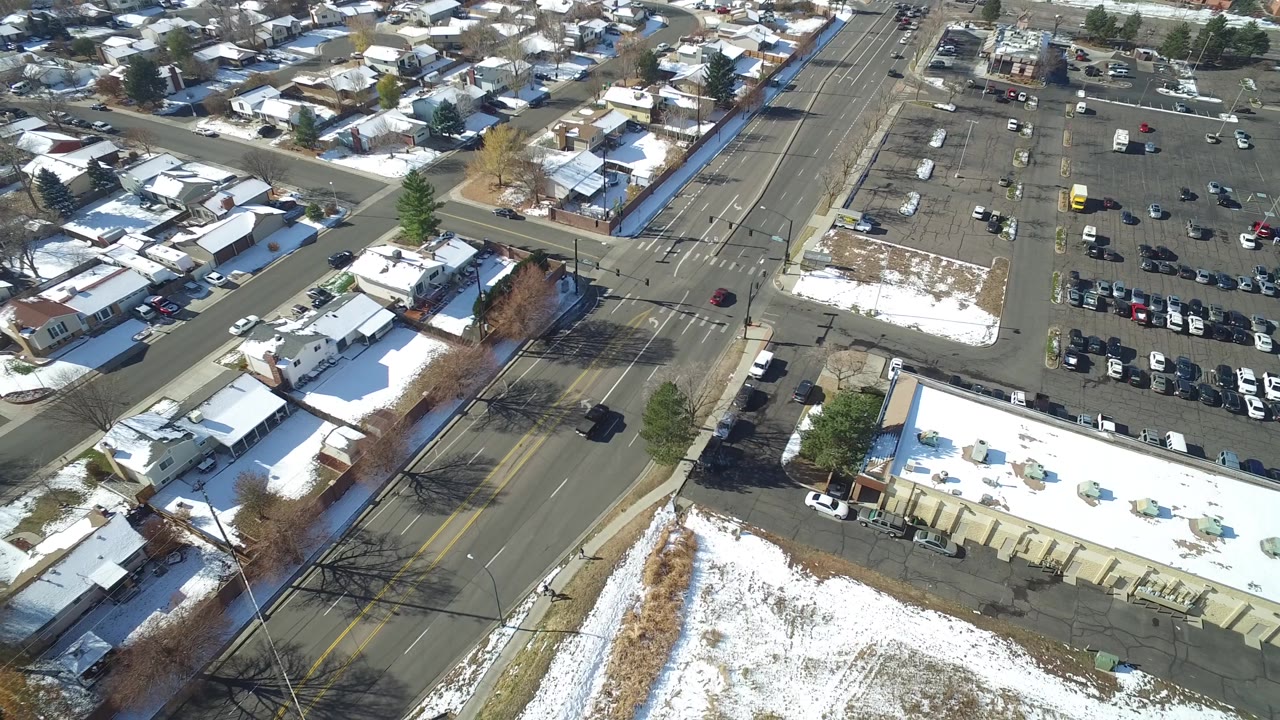 Aerial view in Hidden Lake, Colorado showing a multi-lane road, a large parking area, snow-dusted homes, a low building, and no visible people.
