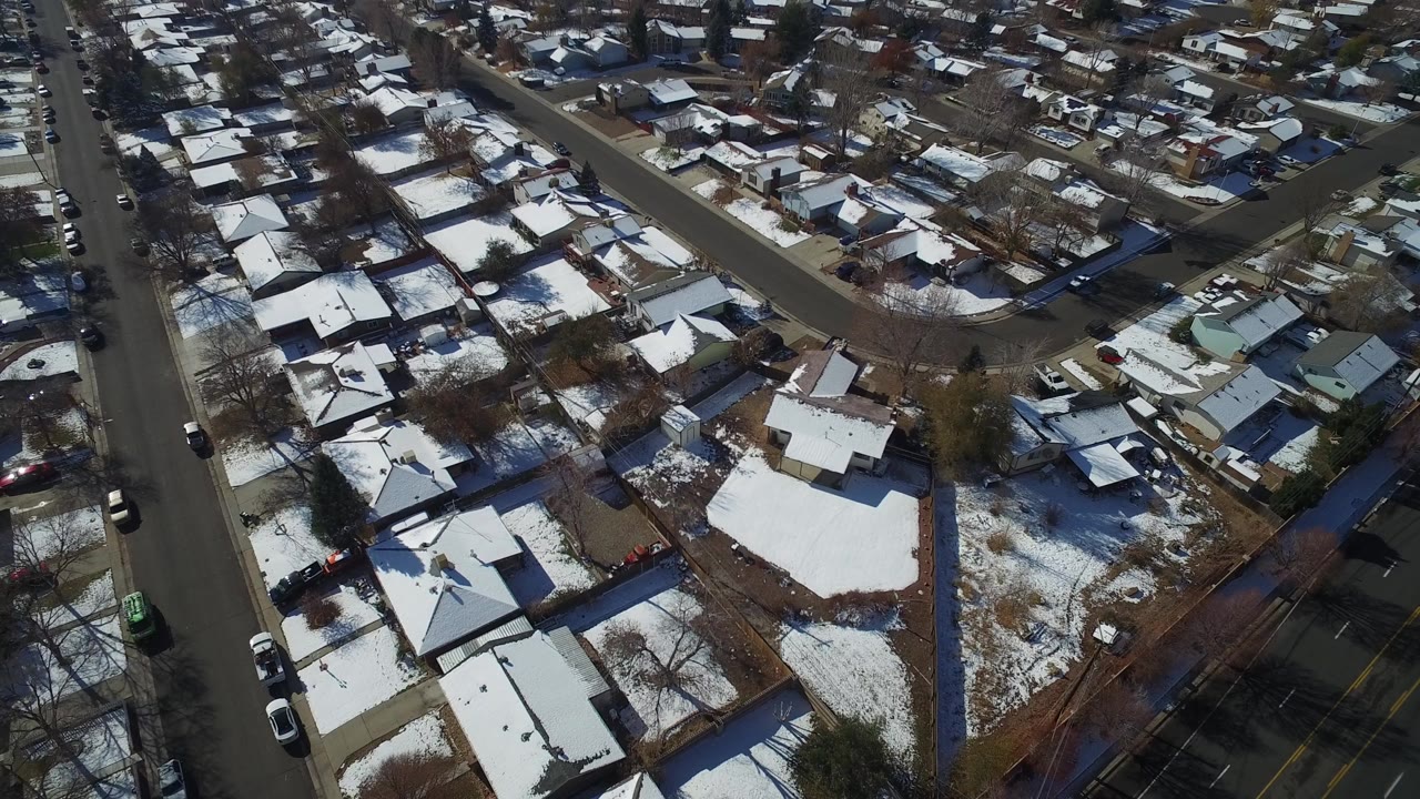 Aerial view over Hidden Lake, Colorado homes with snow on rooftops and lawns, bare trees, parked cars along streets, and no visible people.
