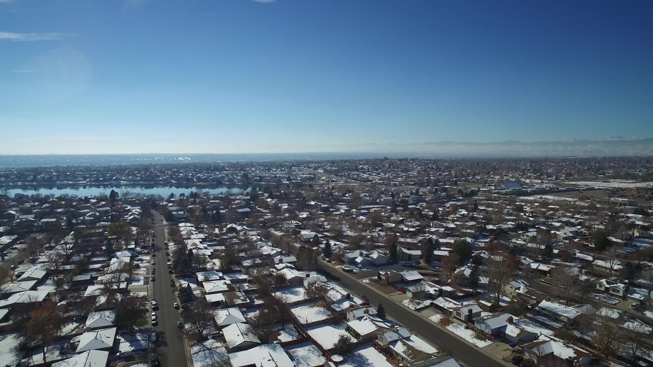 Snowy residential neighborhood seen from above with lake behind it.
