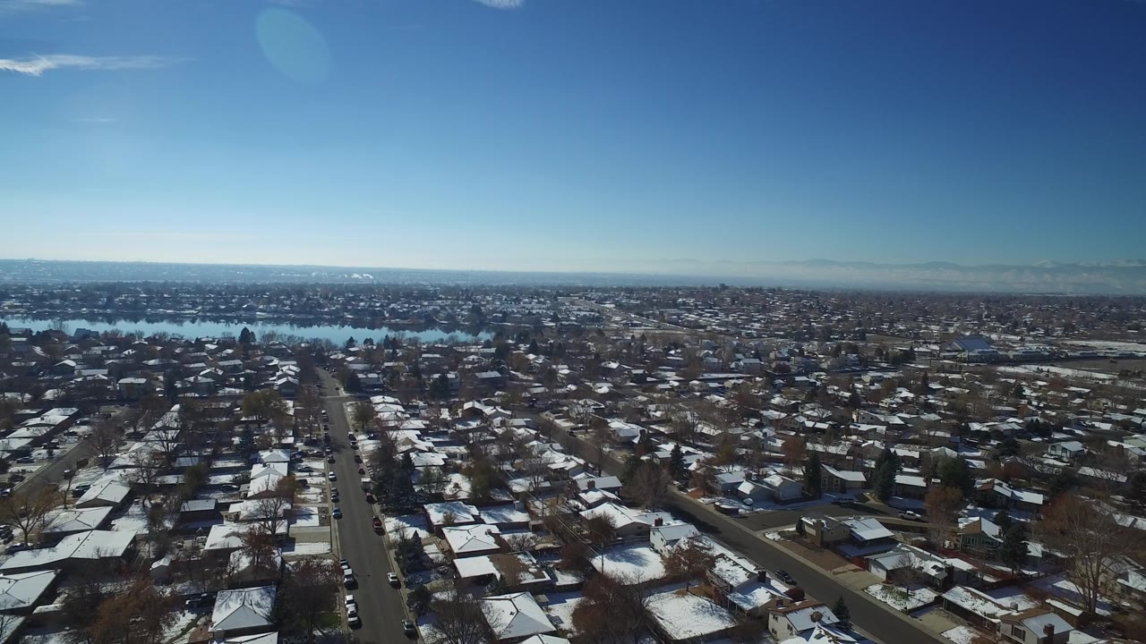 Residential rooftops and roads with snow patches and distant water.