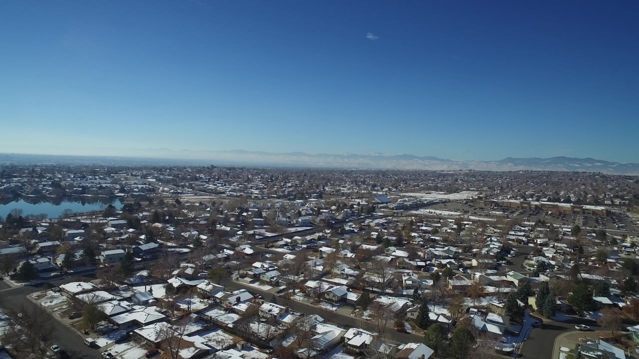 Aerial neighborhood view with snowy houses, trees, and a mountain horizon.