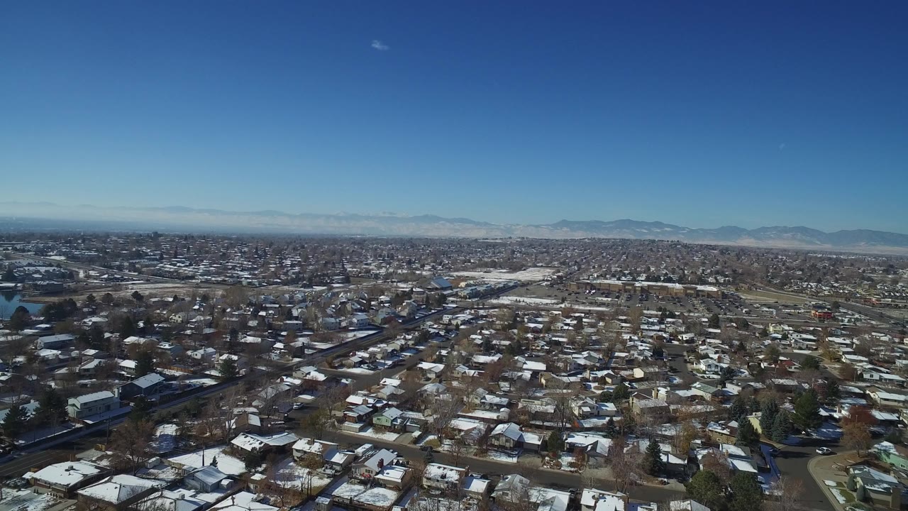 Aerial view over suburban rooftops with distant mountains under blue sky.