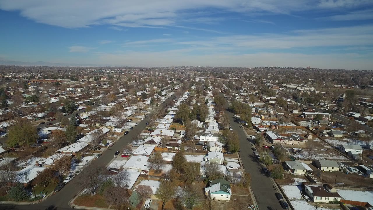 Aerial view in Hidden Lake, Colorado, looking along a central residential street lined with small homes, yards, leafless trees, and snow-covered roof sections.