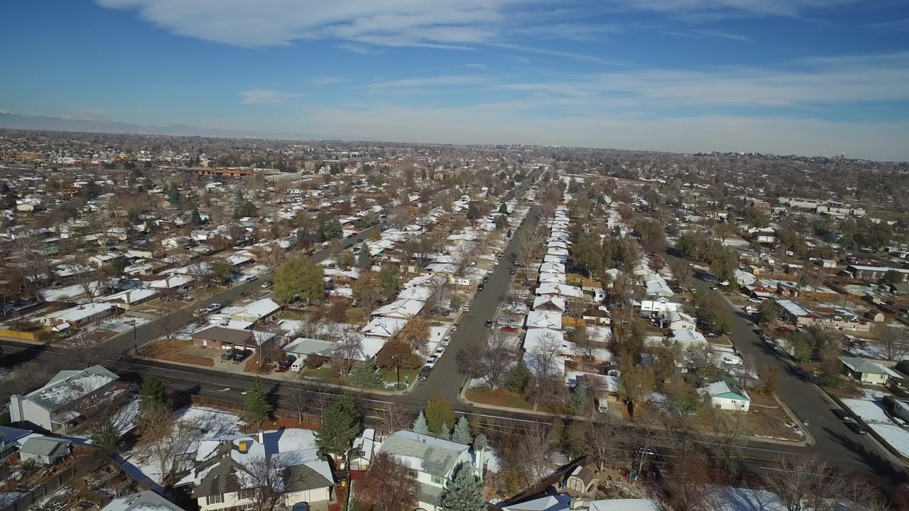 Aerial view across Hidden Lake, Colorado, with a long residential street running through light-colored homes, winter trees, snow patches, and no recognizable people.