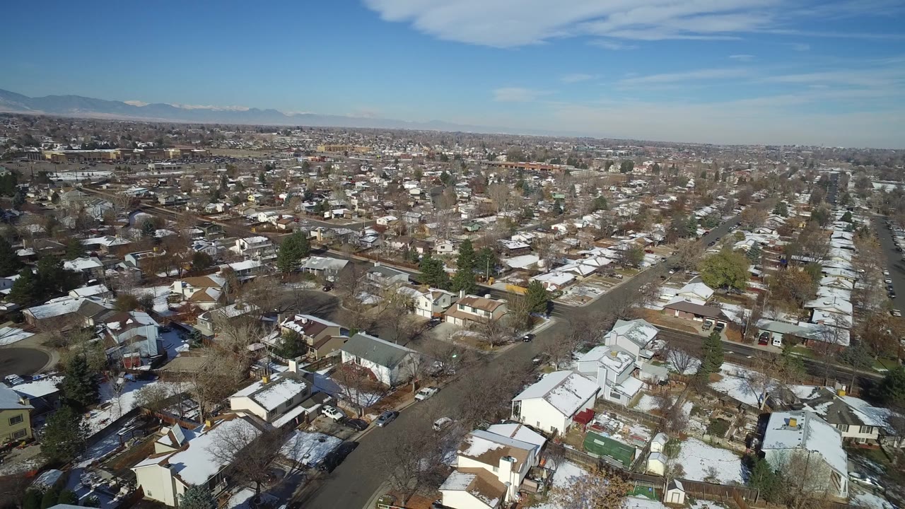 High aerial frame of Hidden Lake, Colorado showing a dense spread of houses, snow patches, leafless trees, streets, distant hills, and no visible people.