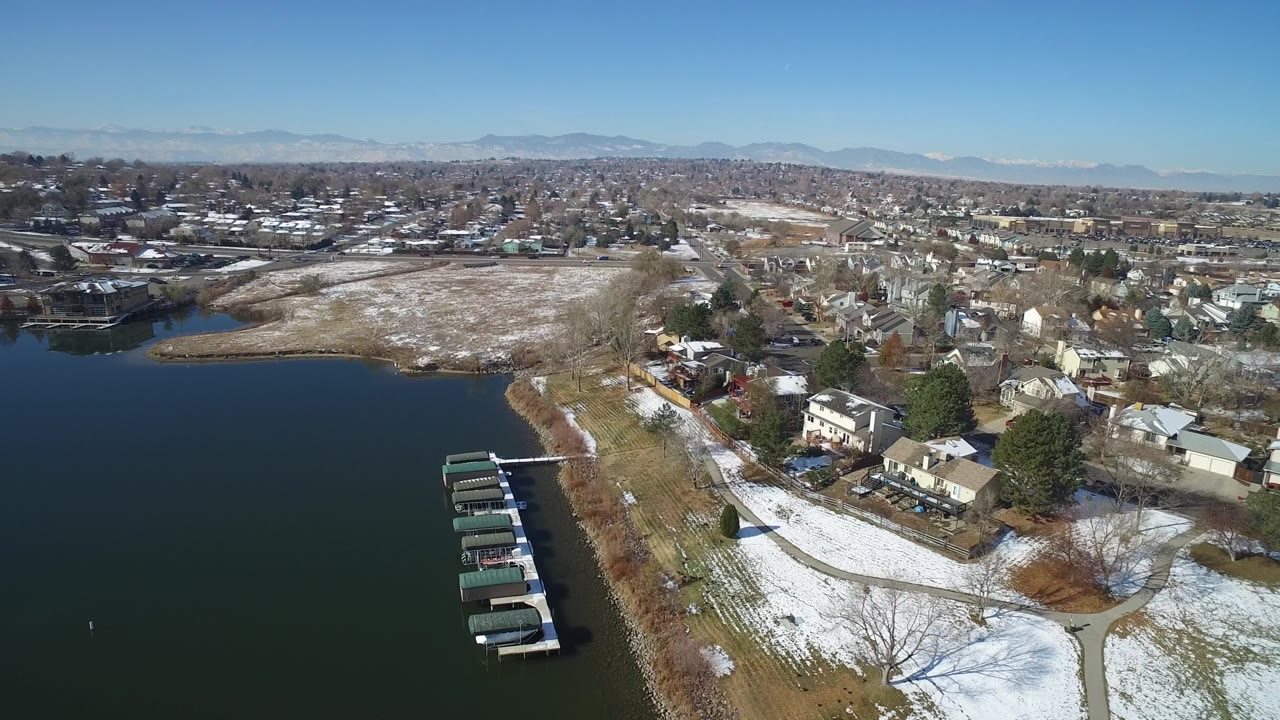 Snowy residential shoreline beside a broad lake and mountain horizon.