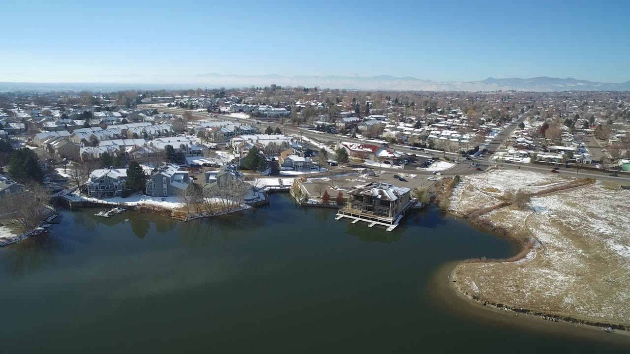 Snowy lakeside neighborhood seen from above with dark water and houses.