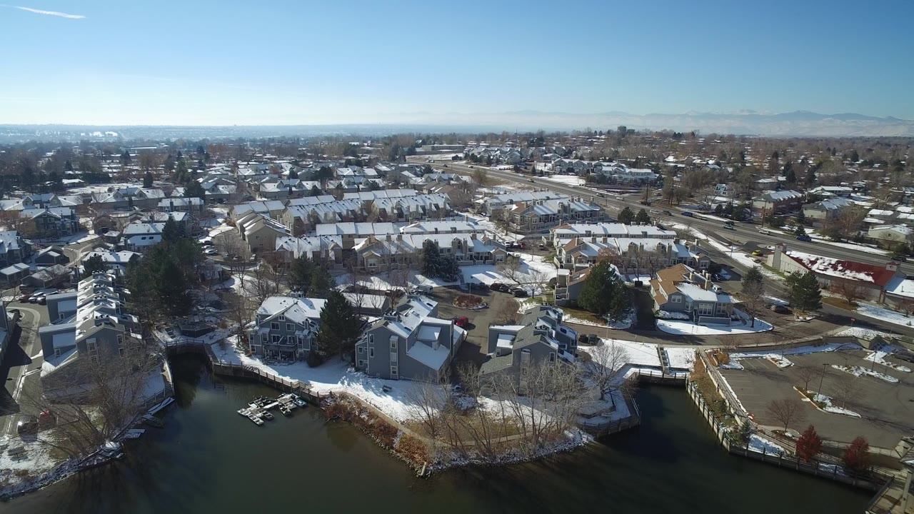 Opening aerial frame over Hidden Lake, Colorado showing snow-dusted homes beside dark water, docks in the foreground, roads through the neighborhood, and no visible people.