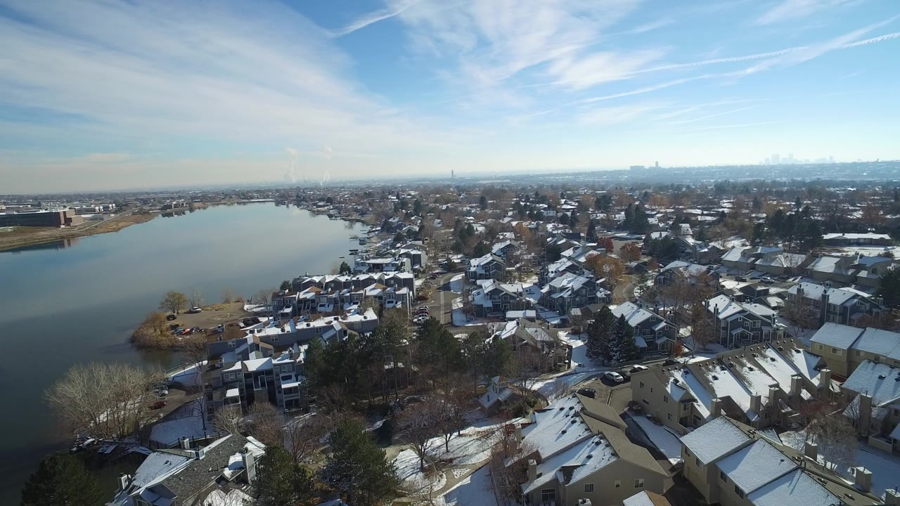Aerial view of a lake beside snow-dusted homes and trees.