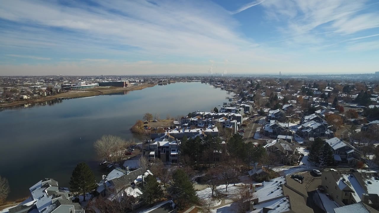 Drone view across a lake toward distant buildings and snowy residential blocks