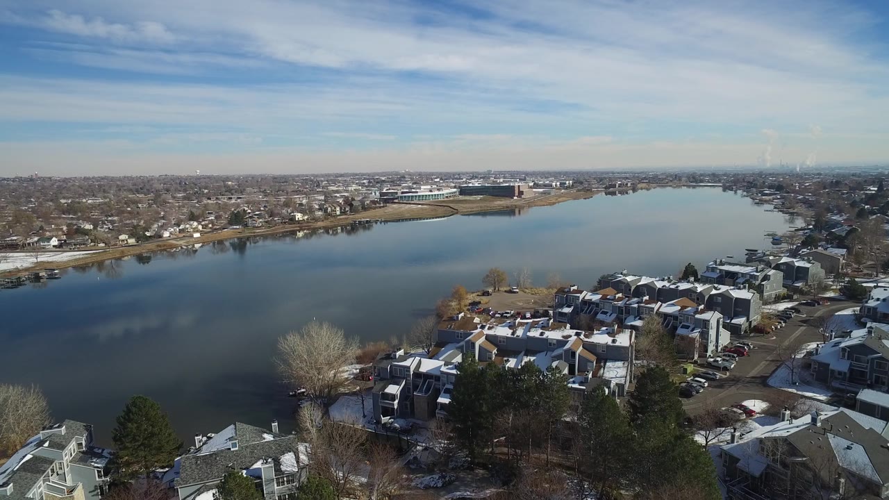 Second frame over Hidden Lake, Colorado, showing more of the lake surface in the center, clustered townhomes below, a shoreline road beyond the water, and no clearly visible people.