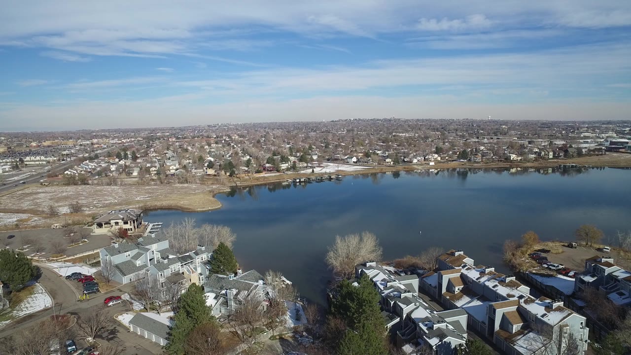 Second frame holds the Hidden Lake, Colorado waterline lower in frame, with more of the distant residential grid and pale winter shoreline visible beyond the lake.