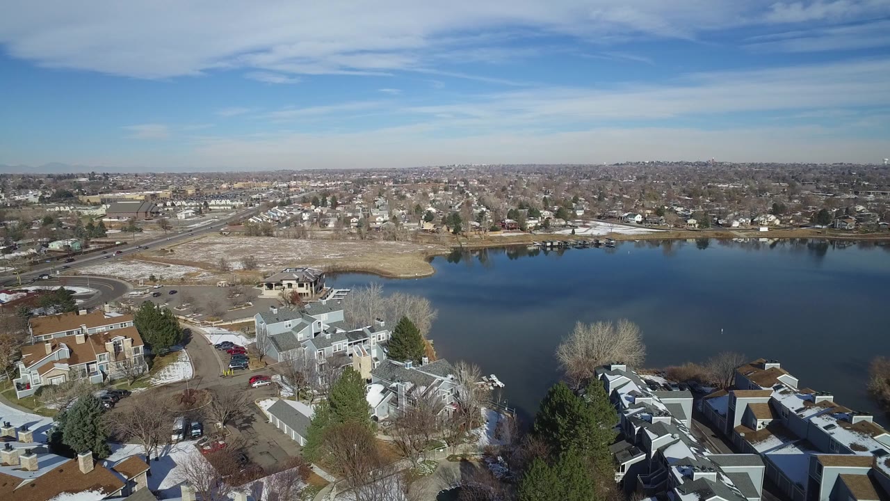 Aerial view over lakeside homes, a blue lake, suburbs, and clear sky.