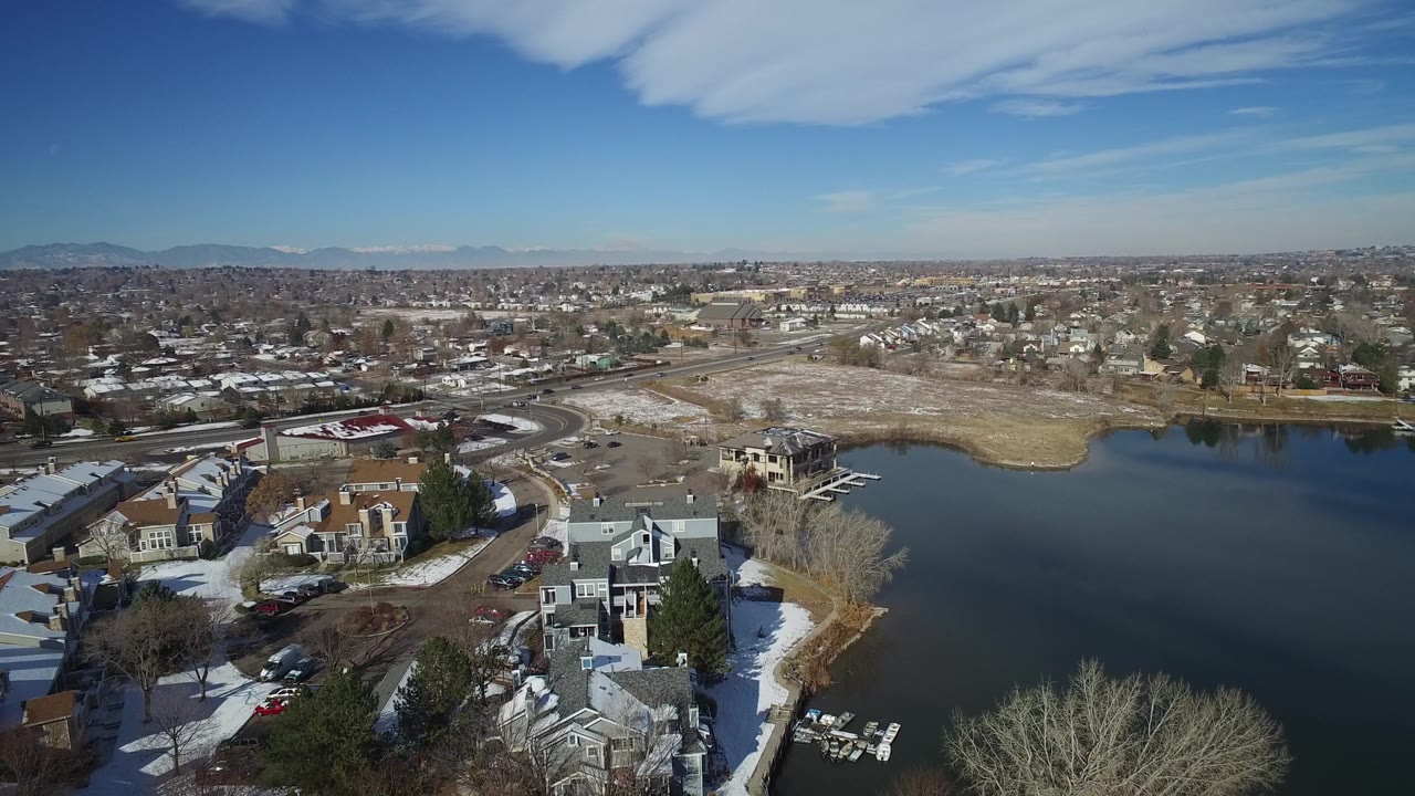 Drone-like view of a lake edge with homes, docks, and a broad city background.
